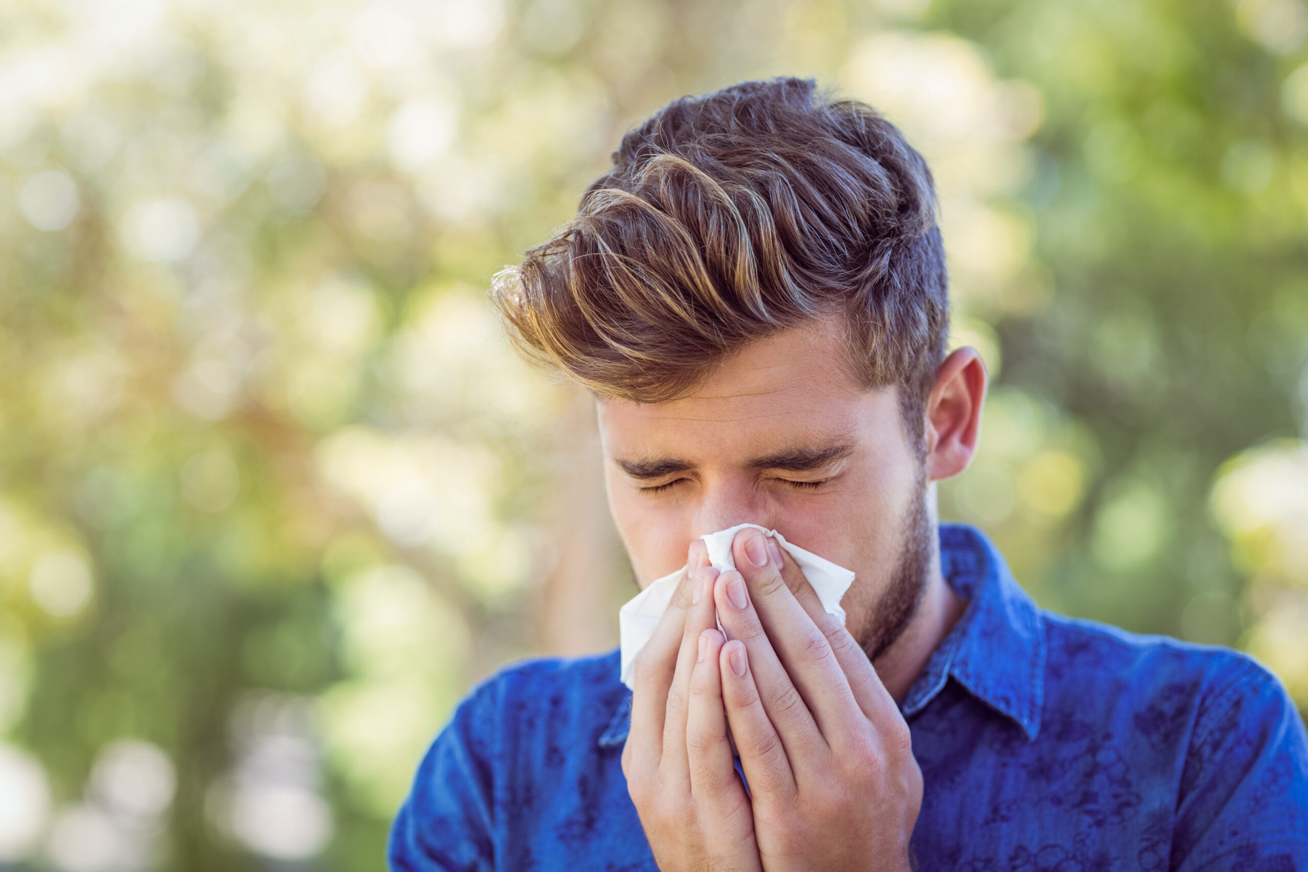 Handsome hipster blowing his nose on a sunny day